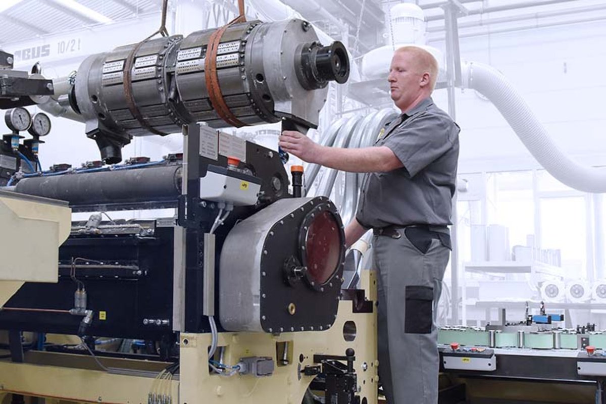 Ein W+D BICMA Techniker hebt mittels Hebezeug einen grossen Falzzylinder in eine Taschentuchmaschine. 